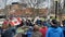 many people watch and stand with flags on a street in front of trees