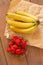 Many red strawberries on glass plate and bunch of bananas on wooden table top view