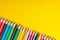 Many sharpened colored pencils laid out on a yellow background. Copyspace