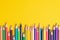 Many sharpened colored pencils laid out on a yellow background. Copyspace