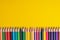 Many sharpened colored pencils laid out on a yellow background. Copyspace