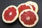 Many sliced fresh grapefruits on black background, top view