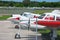 Many small planes parked and lined up on the tarmac at an airport on a sunny afternoon