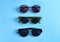 Many stylish sunglasses on blue background, flat lay