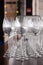 Many transparent crystal wine glasses stand in row on the brown wooden shelves of the rack. Side view. Concept of tasting, banquet