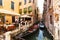 Many visitors in typical tiny cafe in Venice near canal with gondolas and boats