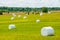 Many white sacks of mown and packed hay laid out on the green field surrounded by scenic landscape