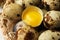 Many whole and cracked quail eggs in wicker bowl, closeup