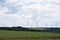 many wind power plants on the hill with the power lines and grain fields below