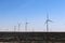 Many wind turbines on the prairie with burned black field in foreground under blue cloudless sky