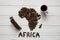 Map of the Africa made of roasted coffee beans laying on white wooden textured background with cup of coffee, toy train