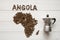 Map of the Angola made of roasted coffee beans laying on white wooden textured background with coffee maker