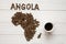 Map of the Angola made of roasted coffee beans laying on white wooden textured background with cup of coffee