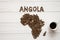 Map of the Angola made of roasted coffee beans laying on white wooden textured background with cup of coffee