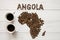 Map of the Angola made of roasted coffee beans laying on white wooden textured background with two cups of coffee