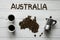 Map of the Australia made of roasted coffee beans laying on white wooden textured background with coffee maker and two coffee cups