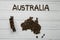 Map of the Australia made of roasted coffee beans laying on white wooden textured background with toy train