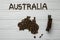 Map of the Australia made of roasted coffee beans laying on white wooden textured background with toy train