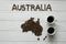 Map of the Australia made of roasted coffee beans laying on white wooden textured background with two coffee cups