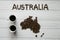 Map of the Australia made of roasted coffee beans laying on white wooden textured background with two coffee cups