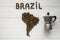 Map of the Brazil made of roasted coffee beans laying on white wooden textured background with coffee maker