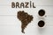 Map of the Brazil made of roasted coffee beans laying on white wooden textured background two cups of coffee