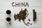 Map of the China made of roasted coffee beans laying on white wooden textured background with toy train and two cups of coffee