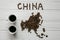 Map of the China made of roasted coffee beans laying on white wooden textured background with two cups of coffee