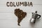 Map of the Columbia made of roasted coffee beans laying on white wooden textured background with coffee maker