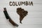 Map of the Columbia made of roasted coffee beans laying on white wooden textured background with toy train