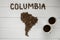 Map of the Columbia made of roasted coffee beans laying on white wooden textured background with two coffee cups