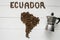 Map of the Ecuador made of roasted coffee beans laying on white wooden textured background with coffee maker