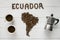 Map of the Ecuador made of roasted coffee beans laying on white wooden textured background with cups of of coffee, coffee maker
