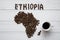 Map of the Ethiopia made of roasted coffee beans laying on white wooden textured background with coffee cup