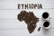 Map of the Ethiopia made of roasted coffee beans laying on white wooden textured background with two coffee cups