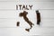 Map of the Italy made of roasted coffee beans laying on white wooden textured background with toy train