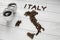 Map of the Italy made of roasted coffee beans laying on white wooden textured background with two cups of coffee