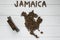 Map of the Jamaica made of roasted coffee beans laying on white wooden textured background with toy train