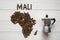 Map of the Mali made of roasted coffee beans laying on white wooden textured background with coffee maker