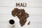 Map of the Mali made of roasted coffee beans laying on white wooden textured background with cup of coffee