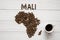 Map of the Mali made of roasted coffee beans laying on white wooden textured background with cup of coffee