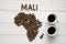 Map of the Mali made of roasted coffee beans laying on white wooden textured background with two cups of coffee
