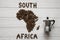 Map of the South Africa made of roasted coffee beans laying on white wooden textured background with coffee maker