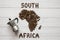 Map of the South Africa made of roasted coffee beans laying on white wooden textured background with coffee maker