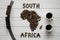 Map of the South Africa made of roasted coffee beans laying on white wooden textured background with toy train and two cups of c