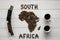 Map of the South Africa made of roasted coffee beans laying on white wooden textured background with two cups of coffee, toy train