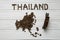 Map of the Thailand made of roasted coffee beans laying on white wooden textured background with toy train