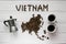 Map of the Vietnam made of roasted coffee beans laying on white wooden textured background with coffee maker and cups of coffee