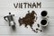 Map of the Vietnam made of roasted coffee beans laying on white wooden textured background with coffee maker and cups of coffee