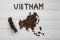 Map of the Vietnam made of roasted coffee beans laying on white wooden textured background with toy train